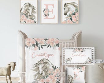 May include: A nursery set featuring a watercolor horse theme. The set includes framed art prints, a crib blanket, a crib bumper, and a decorative pillow. The artwork features a horse surrounded by pink flowers and greenery. The blanket and bumper have the name "Emmalynn" in pink script.