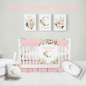 K&ouml;nnte beinhalten: Ein wei&szlig;es Babybett mit einem rosa-wei&szlig;en Blumenbettw&auml;sche-Set. Die Bettw&auml;sche umfasst einen Bettrock, eine Decke und zwei Kissen. Die Decke und die Kissen tragen den Namen "Claudia Rose" und einen goldenen Buchstaben C. Das Babybett ist mit drei gerahmten Drucken mit Schmetterlingen und Blumenmustern verziert.