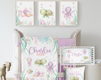 May include: A nursery set featuring a crib, bedding, and wall art with an under-the-sea theme. The set includes a crib, blanket, fitted sheet, and pillow with illustrations of a goldfish, turtle, and octopus in pastel colors. The name "Charlee Ann" is displayed on the blanket and fitted sheet.
