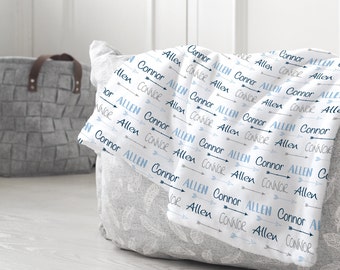 May include: White baby blanket with a repeating pattern of blue and grey arrows with the names "Allen" and "Connor" written on them.