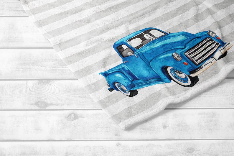 May include: A blue vintage truck illustration on a white and gray striped towel. The truck is a vibrant blue with white tires and chrome details. The towel is folded over a white wooden surface.