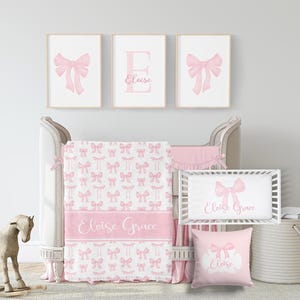 May include: A nursery set with a crib, bedding, and wall art. The set features a pink bow theme. The crib has a white frame with pink accents. The bedding includes a blanket with a bow pattern and the name "Eloise Grace".