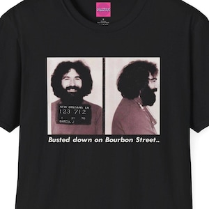 May include: Black t-shirt with a photo of a man's mugshot on the front. The mugshot is from New Orleans, LA and the text "Busted down on Bourbon Street." is printed below the photo.