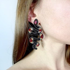 May include: A pair of black beaded earrings shaped like a snake with red and gold accents.