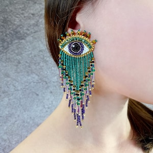 Kolczyki z koralikami „złe oko”. Kolczyki z zielono-fioletowymi, złotymi frędzlami.