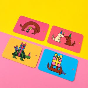 Puede incluir: Cuatro etiquetas de regalo coloridas con ilustraciones de dibujos animados. Una etiqueta presenta un perro marrón con una flor, dos perros con gorros de fiesta, una tortuga con regalos y un perro salchicha que lleva un regalo. Cada etiqueta tiene un pequeño agujero.
