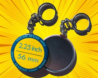 以下が含まれることがあります： 青い縁取りと黄色の中心を持つ、直径5.7cm（56mm）の丸いボタン。ボタンには「Custom Design Here Photo Drawing Logo Words」という文字が書かれています。ボタンは、2つの銀色のリングが付いた銀色のキーチェーンに取り付けられています。