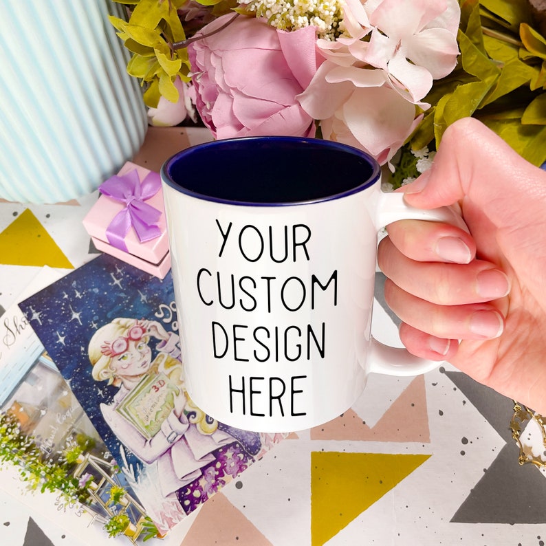 May include: White ceramic mug with a blue rim. The mug has the text "YOUR CUSTOM DESIGN HERE" printed in black.