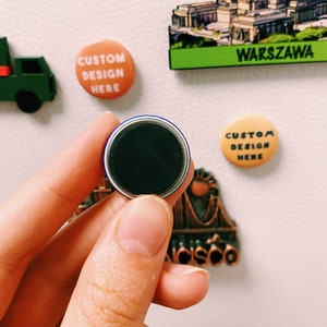 May include: A close-up of a round, black magnet with a blue border. The magnet is being held by a hand. The magnet is a souvenir from a trip to San Francisco.