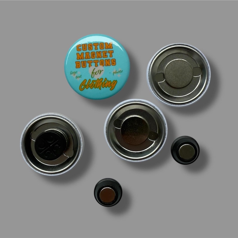 May include: A selection of custom magnet buttons for clothing. The buttons are round with a teal background and orange text that reads "CUSTOM MAGNET BUTTONS for CLOTHING". The image shows the front and back of the buttons.