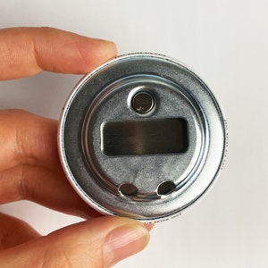 May include: A silver bottle opener with a round, metal design. The opener has a small, circular hole on the top and a rectangular opening on the bottom. The text "Your wings are here" is printed on the side of the opener.