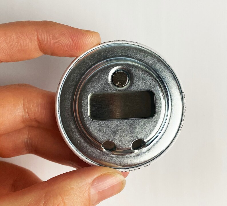 May include: A silver bottle opener with a round, metal design. The opener has a small, circular hole on the top and a rectangular opening on the bottom. The text "Your wings are here" is printed on the side of the opener.