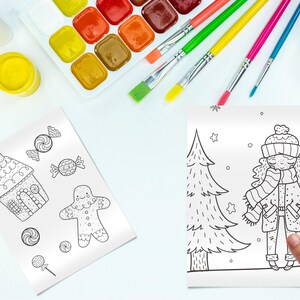 May include: Overhead shot of art supplies including watercolor paints, paintbrushes, and coloring pages. The coloring pages feature holiday-themed illustrations of a gingerbread house, candies, a gingerbread man, a girl in winter clothes, and a Christmas tree.