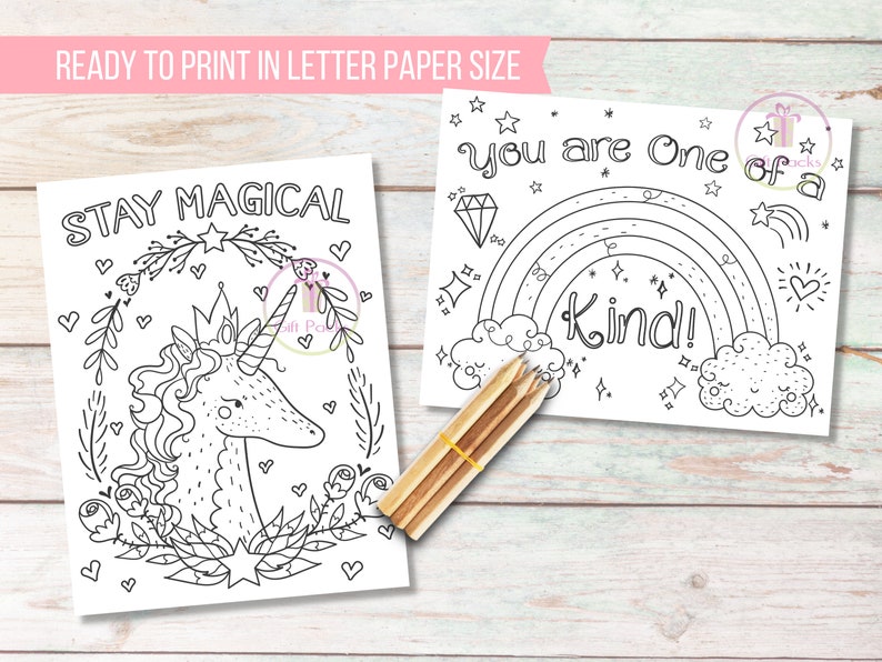 May include: Two black and white coloring pages with the phrases "Stay Magical" and "You are One of a Kind!" are displayed. The first features a unicorn, and the second a rainbow. A bundle of pencils rests on the wooden surface.