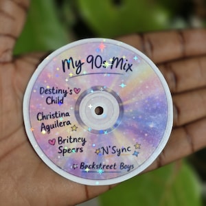 Puede incluir: Una pegatina holográfica con forma de CD con el texto "My 90s Mix". La pegatina incluye artistas como Destiny's Child, Christina Aguilera, Britney Spears, *N Sync y Backstreet Boys. El fondo tiene un diseño de galaxia pastel.