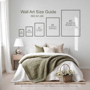 May include: A wall art size guide chart displaying ISO A1 through A5 dimensions in inches and centimetres, positioned above a bed with a green textured throw blanket, pillows, a bedside lamp, and a basket of flowers on the floor.