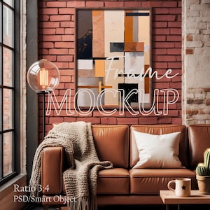May include: A framed abstract art piece with a brown wooden frame hangs on a red brick wall. The artwork features a mix of neutral colors and geometric shapes. A brown leather sofa with a beige throw blanket and white pillow is in front of the wall.