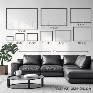 May include: A wall art size guide displays various framed rectangular sizes, including 5"x7", 8"x10", 8"x12", 11"x14", 12"x18", 16"x20", 16"x24", 20"x30", and 24"x36". The guide is displayed above a black leather sectional sofa and a round coffee table. The text "Wall Art Size Guide" is visible.