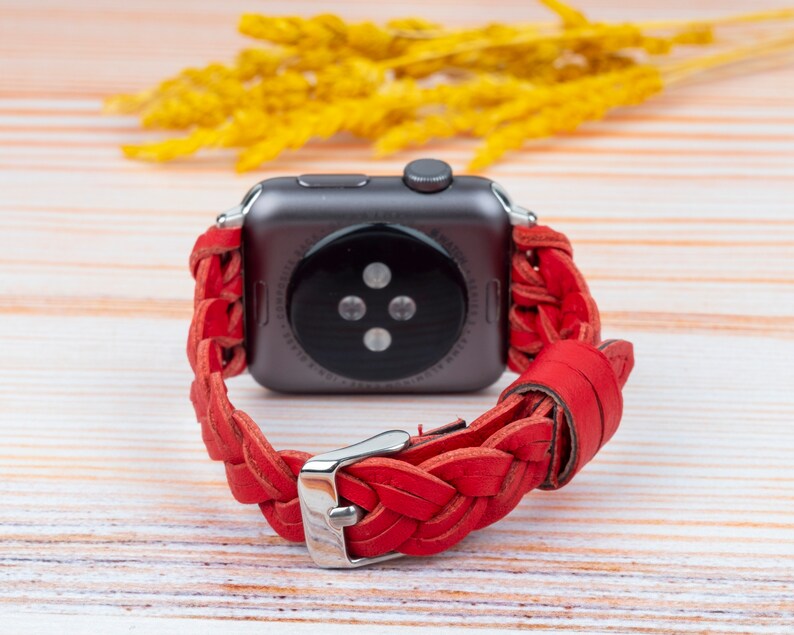 Puede incluir: Pulsera de reloj de cuero trenzado rojo para un Apple Watch. La pulsera est&aacute; tejida con un patr&oacute;n trenzado y tiene una hebilla plateada.