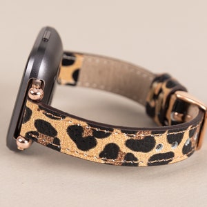 Puede incluir: Un smartwatch negro con una banda de estampado de leopardo. La banda tiene una hebilla y detalles en oro rosa.