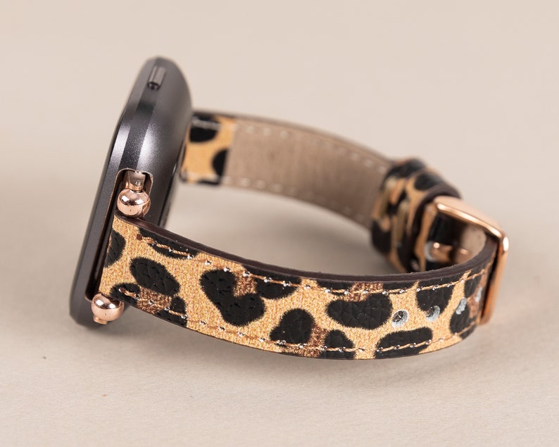 Puede incluir: Un smartwatch negro con una banda de estampado de leopardo. La banda tiene una hebilla y detalles en oro rosa.