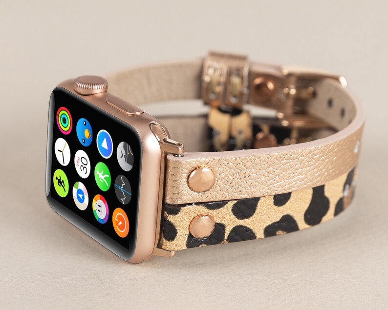 Może przedstawiać: Złoty zegarek Apple Watch z czarno-złotym paskiem ze sk&oacute;ry w panterkę. Tarcza zegarka wyświetla r&oacute;żne ikony aplikacji.