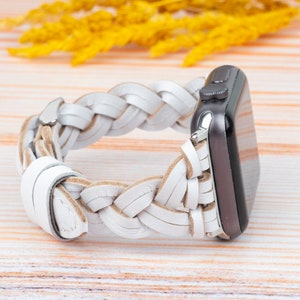 Könnte beinhalten: Weißes geflochtenes Lederarmband für eine Apple Watch. Das Armband ist aus geflochtenem Leder und hat eine silberne Schließe.