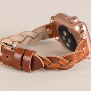 Puede incluir: Una correa de reloj trenzada de cuero marr&oacute;n con un Apple Watch de oro rosa.
