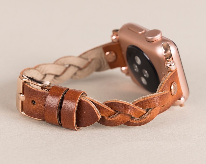 Puede incluir: Una correa de reloj trenzada de cuero marr&oacute;n con un Apple Watch de oro rosa.
