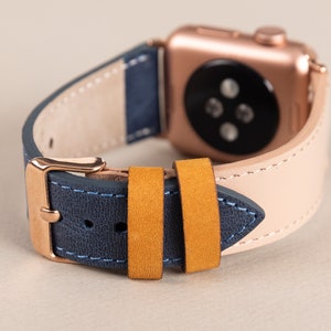 May include: A rose gold Apple Watch with a blue and beige leather strap. The band has a yellow suede strap.
