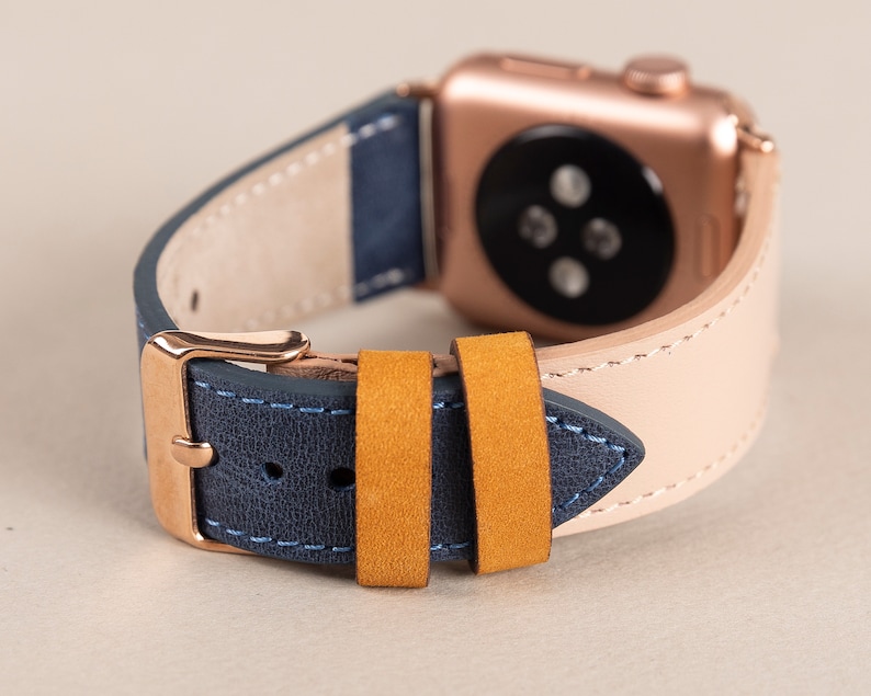 May include: A rose gold Apple Watch with a blue and beige leather strap. The band has a yellow suede strap.