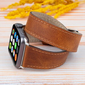 K&ouml;nnte beinhalten: Ein braunes Lederarmband f&uuml;r die Apple Watch mit gen&auml;htem Rand. Das Armband ist um eine silberne Apple Watch mit schwarzem Zifferblatt gewickelt.