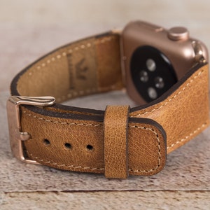 May include: A brown leather watch strap with a rose gold buckle and a stitched edge. The strap is designed for an Apple Watch.