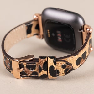 Puede incluir: Un smartwatch de oro rosa con una esfera negra y una correa de cuero con estampado de leopardo.