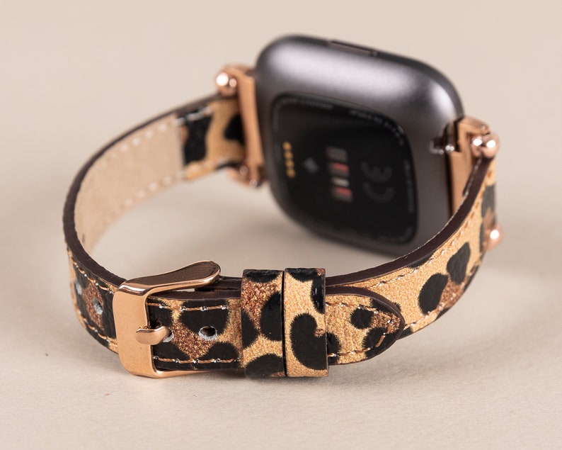 Puede incluir: Un smartwatch de oro rosa con una esfera negra y una correa de cuero con estampado de leopardo.