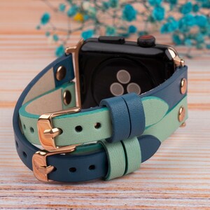 May include: A double-layered watch band in teal blue and light green leather with rose gold hardware. The band is designed for an Apple Watch.