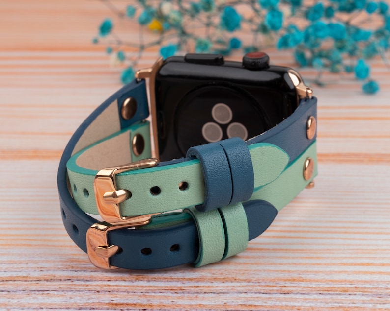 May include: A double-layered watch band in teal blue and light green leather with rose gold hardware. The band is designed for an Apple Watch.