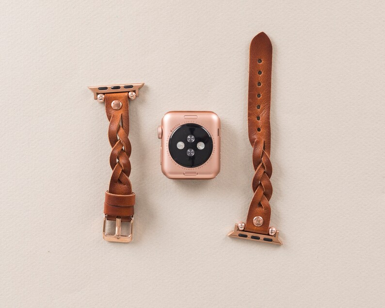 Puede incluir: Dos correas de cuero marr&oacute;n para Apple Watch con herrajes de oro rosa. Una correa es trenzada y la otra es una correa simple.