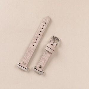 Puede incluir: Dos correas de reloj de cuero rosa claro con hebillas plateadas. Las correas son de cuero texturizado y tienen un dise&ntilde;o sencillo.