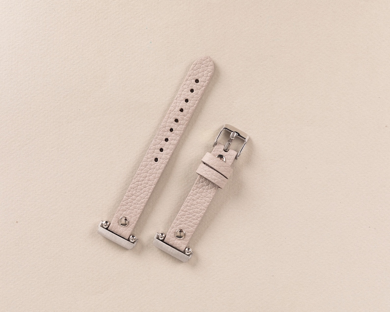 Puede incluir: Dos correas de reloj de cuero rosa claro con hebillas plateadas. Las correas son de cuero texturizado y tienen un dise&ntilde;o sencillo.