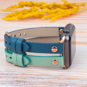 May include: A teal and light green leather watch band with gold accents for an Apple Watch.