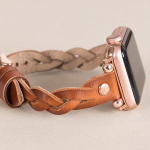 Puede incluir: Un Apple Watch de oro rosa con una banda trenzada de cuero marr&oacute;n. La banda se asegura con un cierre de metal.