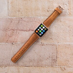 May include: A brown leather watch strap for an Apple Watch. The strap is shown against a brick wall background.
