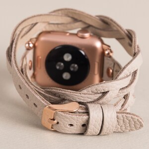 Op de afbeelding: Een beige leren horlogeband met een gevlochten ontwerp. De band is om een ​​rosegouden Apple Watch gewikkeld.