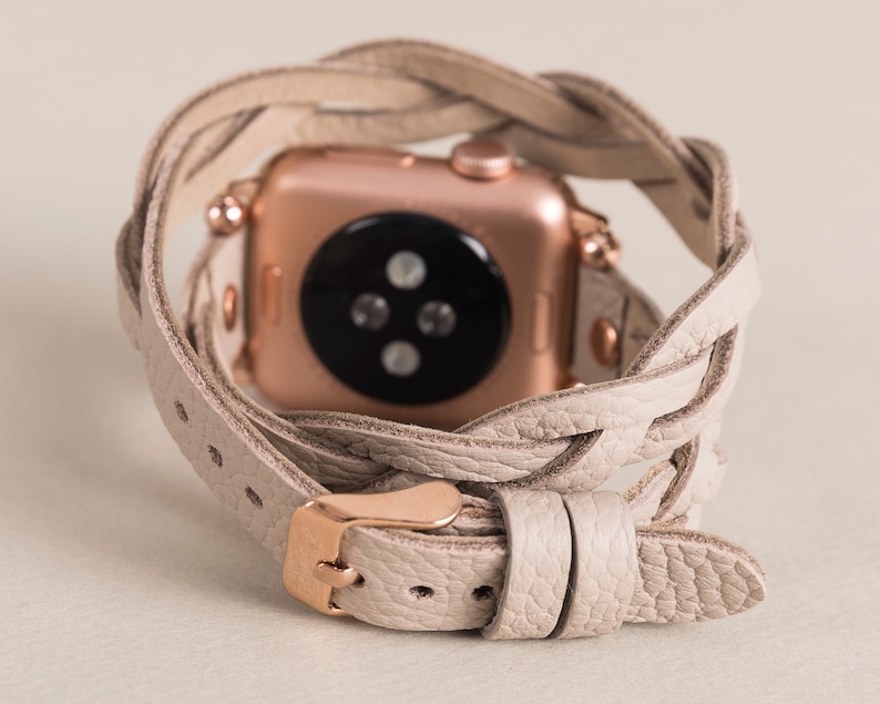 Op de afbeelding: Een beige leren horlogeband met een gevlochten ontwerp. De band is om een ​​rosegouden Apple Watch gewikkeld.