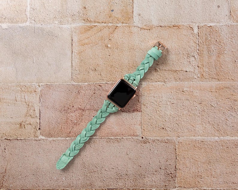 May include: A mint green braided leather watch band with a rose gold buckle and a black smartwatch face. The watch band is made of a soft, flexible leather and is designed to fit a variety of wrist sizes.