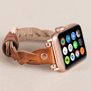 Puede incluir: Un Apple Watch de oro rosa con una correa de cuero marr&oacute;n trenzada. La esfera del reloj muestra una variedad de iconos de aplicaciones.