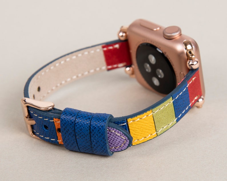 K&ouml;nnte beinhalten: Eine Apple Watch in Ros&eacute;gold mit einem bunten Lederarmband. Das Armband hat Streifen in Blau, Gelb, Gr&uuml;n, Rot und Lila.