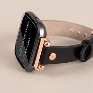 May include: A black smartwatch with a rose gold band and a black leather strap. The screen displays 12,000 steps and 67 bpm.
