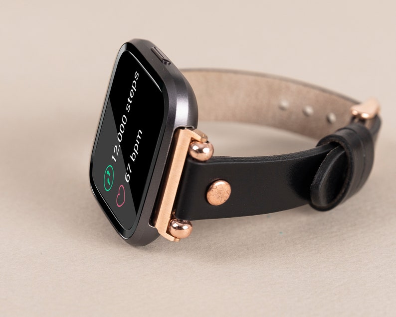 May include: A black smartwatch with a rose gold band and a black leather strap. The screen displays 12,000 steps and 67 bpm.